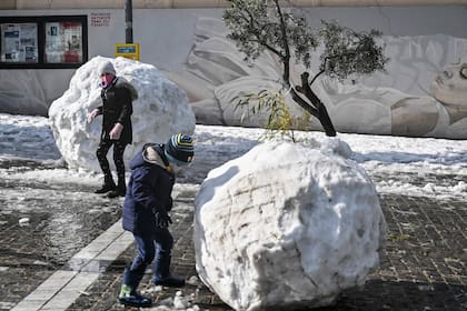 Los niños juegan con enormes bolas de nieve en Atenas el 25 de enero de 2022, después de una tormenta de nieve que interrumpió el tráfico en la capital griega