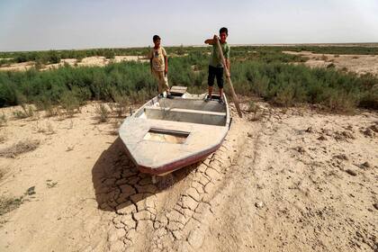 Los niños se paran en un bote varado en el suelo seco de lo que fue el lago Hamrine en la provincia iraquí de Diyala