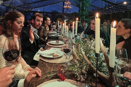 Los novios (a la izquierda de la imagen) en una de las largas mesas para veinte personas, decoradas con ramas de pino y candelabros de asta. El plato principal fue trucha con vegetales.