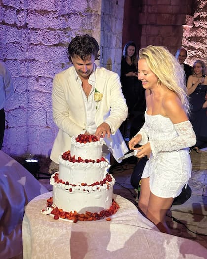 Los novios cortan la torta de tres pisos decorada con buttercream y frutillas.