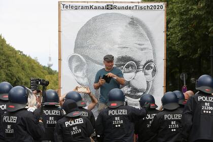 Los oficiales de policía hablan con un manifestante frente a un gran retrato de Mahatma Gandhi en una protesta contra las regulaciones gubernamentales sobre el coronavirus celebrada en Berlín, Alemania, el 30 de agosto de 2020