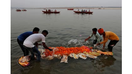 Los parientes sumergen un cuerpo en el río Ganges antes de la cremación en Varanasi