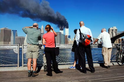 Los peatones en el paseo marítimo de Brooklyn, Nueva York, miran a través del East River hacia las torres del World Trade Center en llamas