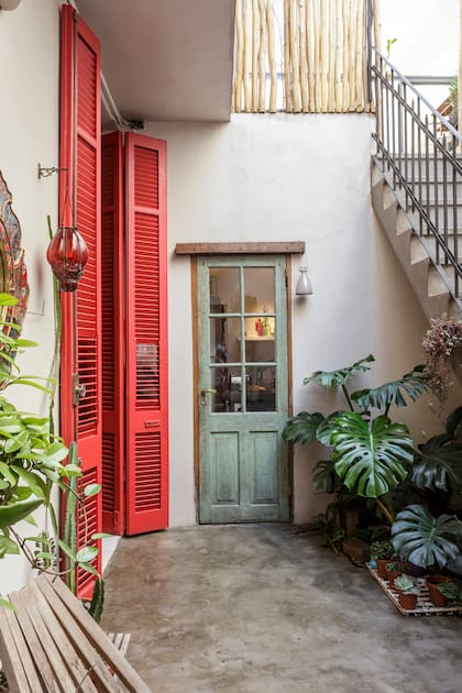Los postigones rojos acentúan los tonos sobrios de este típico patio de entrada y distribución de un PH en Flores.