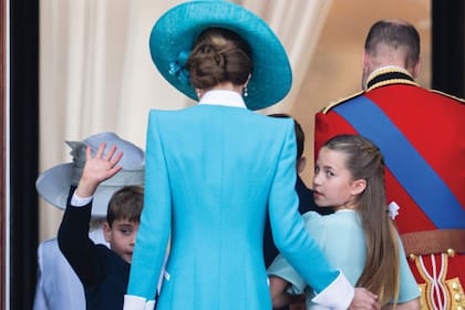 Los príncipes de Gales salen del balcón detrás de los Reyes. La multitud aún los vitoreaba cuando Charlotte se dio vuelta para dar una última mirada y Louis aprovechó para volver a saludar. La imagen también permite apreciar el elaborado peinado recogido de Kate.