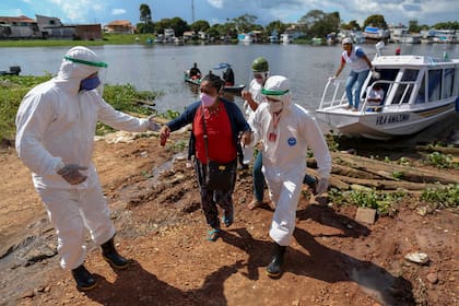 Los profesionales de la salud ayudan a los pacientes con síntomas del nuevo coronavirus traídos en una ambulancia en bote desde la comunidad de Vila Amazonia a su llegada a Parintins, estado de Amazonas, Brasil