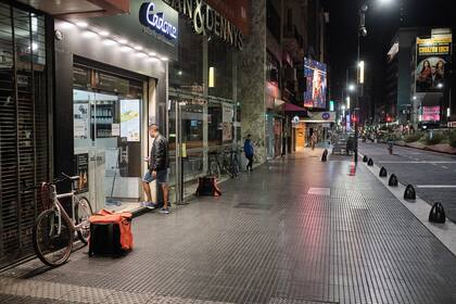 En medio de avenida Corrientes vacía un repartidos espera un pedido en la puerta de un local de comidas