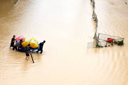 Los residentes mueven sus pertenencias a través de una calle inundada en Zhengzhou, en la provincia de Henan, en el centro de China. El ejército de China ha volado una presa para liberar las aguas que amenazan una de sus provincias más densamente pobladas. ya que el número de muertos en inundaciones generalizadas aumentó a más de dos docenas
