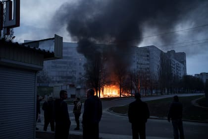 Los residentes permanecen fuera de sus apartamentos mientras las tiendas arden después de un ataque ruso en Kharkiv, Ucrania, el lunes 11 de abril de 2022.