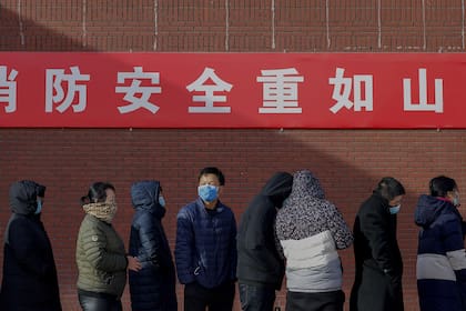 Los residentes que usan máscaras faciales esperan en una cola para hacerse la prueba del coronavirus en Pekín el 29 de diciembre de 2020