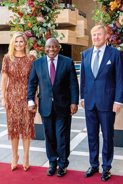 Los reyes de los Países Bajos posan con el presidente de Sudáfrica, Cyril Ramaphosa, en el segundo día de su visita al país. Y Máxima causó sensación con un look de lo más llamativo: top manga corta y cuello redondo + falda tubo de lentejuelas color cobre y en forma de gotas que simulan flecos, firmado por Natan, zapatos de acabado cobrizo brillante de Gianvito Rossi y pendientes con forma de pluma color aluminio de la firma Jar. El segundo toque de brillo lo puso su reloj de diamantes de Patek Philippe. 