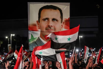 Los sirios ondean banderas nacionales y un gran retrato de su presidente mientras celebran en las calles de la capital, Damasco, un día después de una elección programada para darle al actual presidente Bashar al-Assad un cuarto mandato, el 27 de mayo de 2021