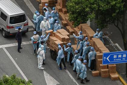 Los trabajadores con equipo de protección apilan cajas con comida sobre un carrito para entregar en un vecindario durante un bloqueo de Covid-19 en el distrito de Jing'an, en Shanghai. (Photo by Hector RETAMAL / AFP)