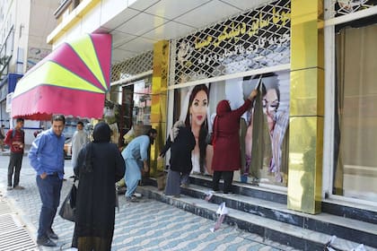 Los trabajadores de un salón de belleza quitan fotografías de mujeres de la pared en Kabul el 15 de agosto de 2021.