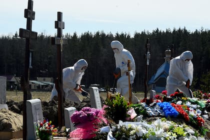 Los trabajadores del cementerio que usan equipo de protección entierran a una víctima de coronavirus en un cementerio en las afueras de San Petersburgo el 6 de mayo de 2020