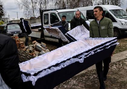 Los trabajadores traen ataúdes donde se transportan los cuerpos para su identificación por parte del personal forense y los agentes de policía en el cementerio de Bucha, al norte de Kiev