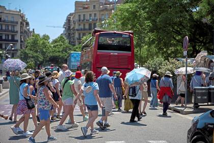 Los turistas caminan, algunos de ellos usando paraguas para protegerse del sol, en un día caluroso en Barcelona, España