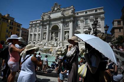 Los turistas se protegen con sombreros y paraguas en la Fontana de Trevi durante una ola de calor en Roma, el 21 de agosto de 2023.