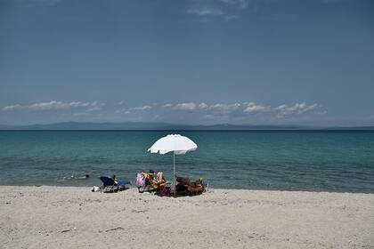 Los turistas se sientan bajo una sombrilla en una playa en Pefkochori en la península de Halkidiki, Grecia, el 20 de junio de 2020