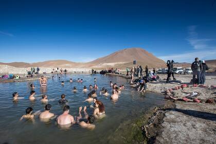 Los turistas se tientan con el chapuzón en la pileta de agua termal al lado de los géiseres.