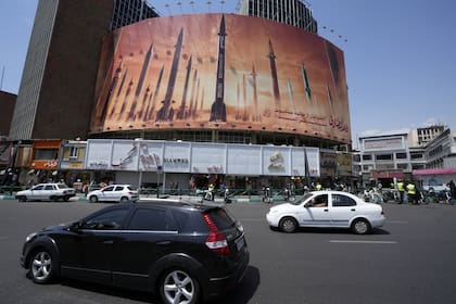 Los vehículos pasan junto a un cartel anti-israelí que muestra misiles siendo lanzados, en una plaza en el centro de Teherán, Irán, el viernes 19 de abril de 2024. 