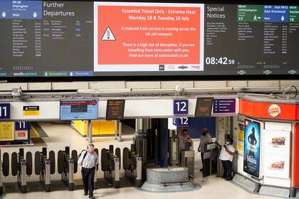 Los viajeros caminan bajo un tablero de mensajes que advierte a la gente de las interrupciones por el calor extremo en la estación de Victoria en Londres el 18 de julio de 2022.