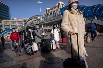 Los viajeros con barbijos caminan hacia la entrada de la estación de tren de Pekín