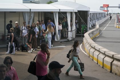 Los viajeros se protegen del sol mientras esperan en largas colas bajo carpas blancas para embarcar en el aeropuerto de Schiphol de Ámsterdam, Holanda, el martes 21 de junio de 2022. 