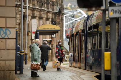 Los viajeros usan tapabocas mientras esperan en una parada de tranvía en Sheffield, South Yorkshire, el 21 de octubre de 2020, antes de que entren en vigor nuevas medidas de bloqueo a medida que aumenta el número de casos de coronavirus