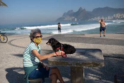 Lucía y su perro Jujuba se sientan en la playa de Arpoador, en medio de la pandemia de coronavirus en Río de Janeiro, Brasil