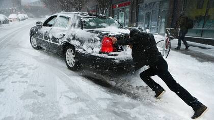 Un hombre empuja un coche atascado en la nieve