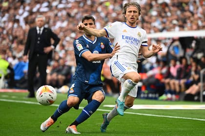 Luka Modric lleva la pelota en el partido ante Espanyol que selló el título; detrás, el DT Carlo Ancelotti observa su obra