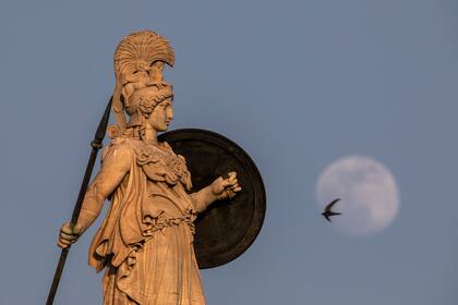 La luna detrás de la estatua de la antigua diosa griega de la sabiduría, Atenea, en lo alto del edificio de la Academia de Atenas