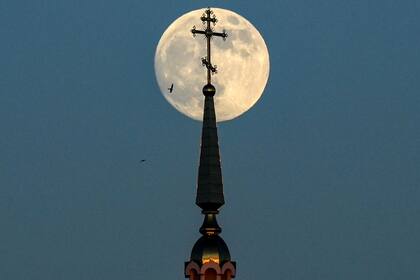 La luna llena se ve detrás de una cruz de una iglesia ortodoxa en la ciudad de Rossosh
