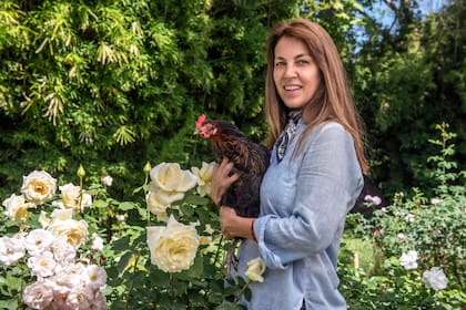 Madeleine, contra un fondo de rosas, junto a una de sus gallinas INTA.