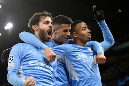 Manchester City's Brazilian striker Gabriel Jesus (R) celebrates with Manchester City's Portuguese midfielder Bernardo Silva (L) and Manchester City's Portuguese defender Joao Cancelo (C) after scoring their second goal during the UEFA Champions League Group A football match between Manchester City and Paris Saint-Germain at the Etihad Stadium in Manchester, north west England, on November 24, 2021. (Photo by Oli SCARFF / AFP)