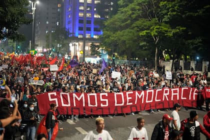 Manifestantes marchan con una bandera que dice "Somos democracia" durante una protesta para reclamar la protección de la democracia del país, en San Pablo, Brasil, el lunes 9 de enero de 2023. (AP Foto/Andre Penner)