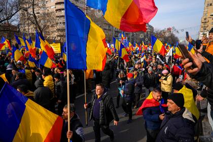 Manifestantes ondean banderas de Rumania durante una marcha organizada por la derechista Alianza por la Unidad de los Rumanos (AUR) para exigir elecciones libres después de que la Corte Constitucional de Rumania anuló la primera vuelta de los comicios presidenciales de diciembre pasado, el domingo 12 de enero de 2025, en Bucarest, Rumania. (AP Foto/Vadim Ghirda)