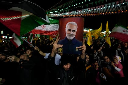 Manifestantes ondean banderas iraníes y palestinas mientras uno de ellos sostiene un cartel con al imagen del fallecido general de la Guardia Revolucionaria Iraní Qassem Soleimani, asesinado en un ataque estadounidense en 2020 durante su manifestación contra Israel para condenar la muerte de miembros de la Guardia Revolucionaria en Siria, en la plaza Felestin de Teherán, el 1 de abril de 2024. (AP Foto/Vahid Salemi)