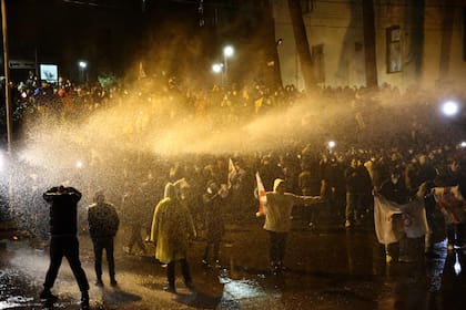 Manifestantes son rociados por un cañón de agua durante los enfrentamientos con la policía antidisturbios cerca del Parlamento georgiano en Tiflis a última hora del 8 de marzo de 2023.