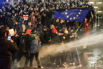 Manifestantes sostienen una bandera de la Unión Europea mientras son rociados por un cañón de agua durante los enfrentamientos con la policía antidisturbios cerca del parlamento georgiano en Tiflis el 7 de marzo de 2023. 
