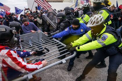 Manifestantes violentos partidarios de Trump agarran una barrera policial en el Capitolio en Washington el 6 de enero