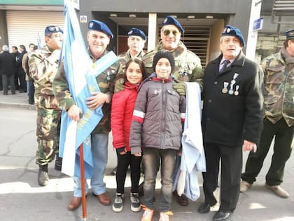 Marcelo Morganti junto a dos de sus hijos, Carla y Julián. A la izquierda, el VGM Daniel Fernández condecorado por sus acciones de guerra el 21 de mayo durante el desembarco británico en San Carlos, donde abatió -junto a sus compañeros- dos helicópteros Gazelle. Portando la bandera, el VGM Oscar Bauchi, soldado del Batallón de Comunicaciones 181. (Cortesía Mariana Morganti).