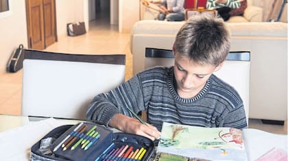 Marcos Garcilazo, de 12 años, pinta un libro que hizo él en la escuela Waldorf; una de sus hermanas, atrás, usa el celular