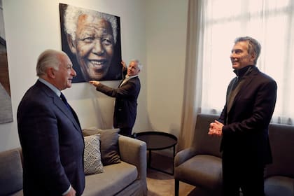 Mauricio Macri charla con Norberto Frigerio de LA NACION, mientras el artista Javier de Aubeyzon sostiene el retrato de Mandela