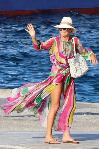 Máxima, radiante, en una foto más amplia que la imagen de apertura de esta nota: lleva un kaftan de gasa de seda de la firma Pucci, que deja traslucir un traje de baño de dos piezas, con cartera de crochet de Twinset, sombrero y anteojos. Apenas desembarcó de su barco, Alma, se puso ojotas