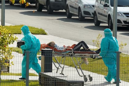 Médicos especialistas con equipo de protección transportan a una persona en camilla fuera de un hospital en Moscú