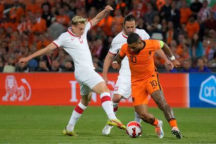 Memphis Depay, que desvió un penal en el final del partido, intenta dejar atrás a Szymon Zurkowski