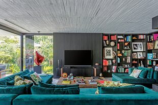 El fondo de la biblioteca tiene el mismo revestimiento que la pared donde se apoya el televisor. Hecho a medida, más profundo que lo habitual, el sillón se tapizó en terciopelo y se lo combinó con almohadones de motivos botánicos.