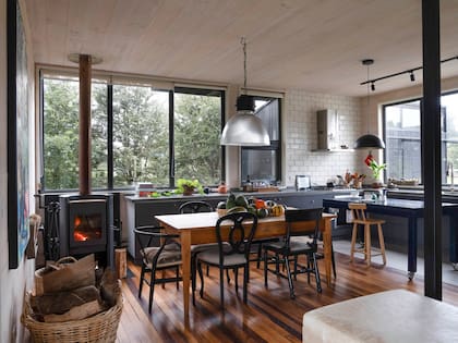 Mesa de comedor de madera de mañío, comprada en un anticuario de Puerto Varas, Chile. Las sillas son un rejunte de piezas vintage, unificadas con pintura negra. En el sector de la isla, resuelto con una mesa alta, el piso de madera se reemplazó con un porcelánico para protegerlo del agua.